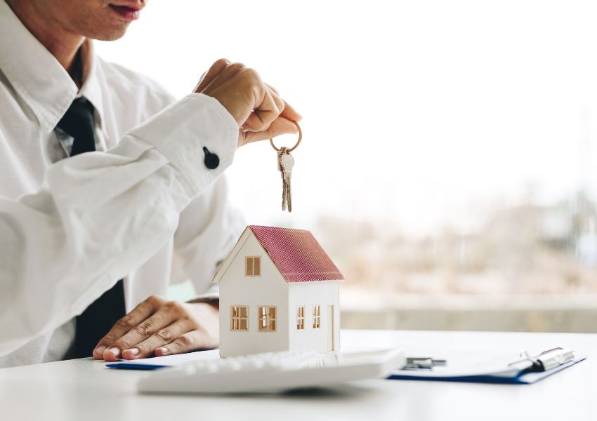 person in a white shirt and black tie holding up a keys with a house figurine on their desk